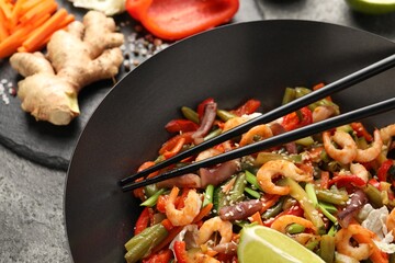 Shrimp stir fry with vegetables and chopsticks in wok on grey table, closeup