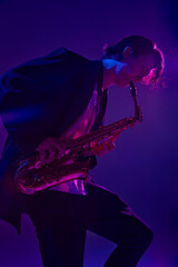 Young man, talented, charismatic solo player in black suit playing sax in vibrant pink neon light...