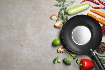 Empty iron wok surrounded by raw ingredients on grey table, flat lay. Space for text