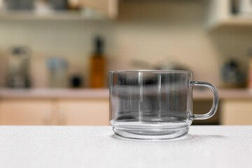 Empty glass cup sitting on laminated kitchen benchtop, Cupboards and cooking appliances in background.