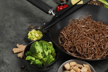 Wok with noodles, chicken and other products on grey table