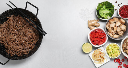Wok with noodles, chicken and other products on light grey table, flat lay. Space for text