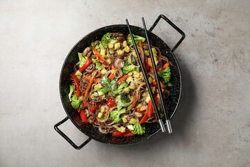 Stir-fry. Tasty noodles with meat in wok and chopsticks on grey textured table, top view