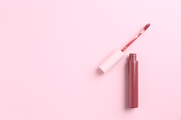 Bright lip gloss and applicator on pink background, top view. Space for text