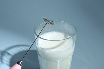 Mini mixer (milk frother) and whipped milk in glass on light blue background, closeup