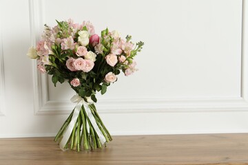 Beautiful bouquet of fresh flowers on wooden table near white wall, space for text