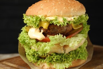 Burger with delicious patty on wooden table against dark background, closeup