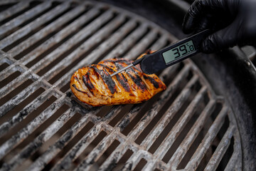 Juicy chicken on a grill checked with professional grill thermometer by cook wearing black rubber cooking gloves during grill season