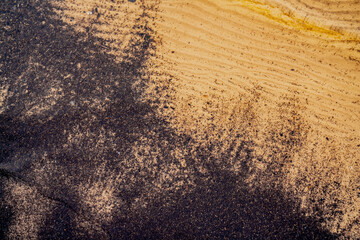 Black mud flowing in the water of yellow sea sand. Mixing good and bad in nature