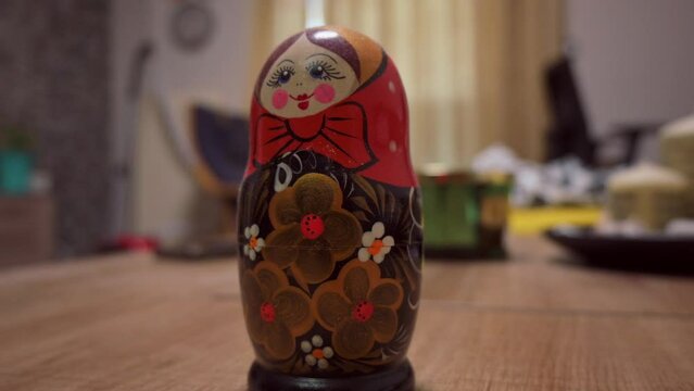 Zoom out camera movement video of a babushka doll placed on a table inside a house.