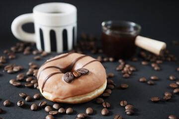 Caramel donut with coffee decor next to a cup with black coffee and a glass ladle with coffee on a dark background