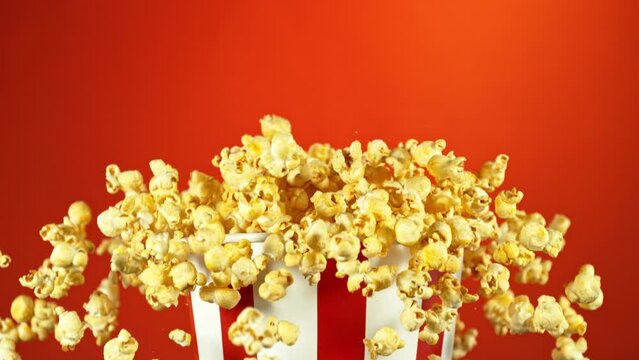 Super Slow Motion of Exploding popcorn from Bucket. Isolated on Red Background. Studio Shot of Flying Food. Filmed on High Speed Cinema Camera, 1000fps. Speed Ramp Effect.