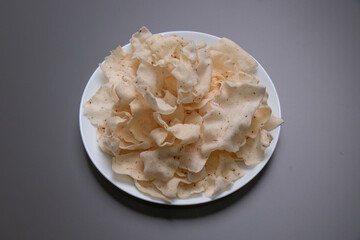 Shiitake Mushroom Crackers on white dish and grey background which consisting of shiitake mushrooms, tapioca starch, salt, ground pepper, made into sheets and then fried.