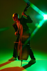 Double bass player performing contemporary jazz composition in red-green neon light against...
