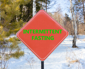 Intermittent fasting symbol. Concept words Intermittent fasting on beautiful red road sign. Beautiful forest snow blue sky background. Healthy lifestyle intermittent fasting concept. Copy space.
