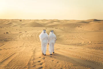 Gordijnen Two arab men wearing traditional emirati clothing in the desert of Dubai - Middle-eastern adult males portrait © oneinchpunch