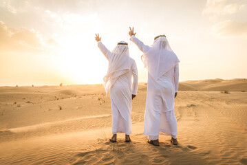 Two arab men wearing traditional emirati clothing in the desert of Dubai - Middle-eastern adult males portrait
