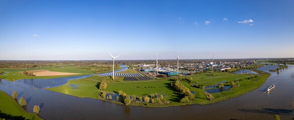Dutch landscape panorama of wind turbine and solar panels with waterway intersection of river IJssel and Twentekanaal against blue sky. Aerial sustainability circular economy concept The Netherlands.