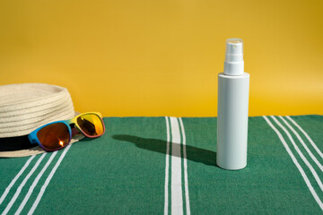 Blank white sunscreen bottle sun hat sunglasses on green Turkish beach towel in direct sunlight....