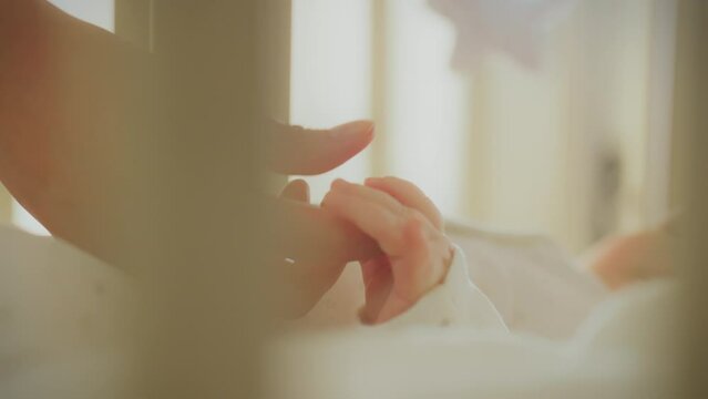 In a quiet children's room, a mother tenderly holds her daughter's hand, filled with love and tenderness. A happy mother gently holds the hand of her baby in the crib, expressing her love and care