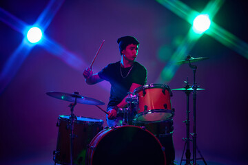 Fototapeta na wymiar Contemporary drummer playing with joy in pink-purple stage lighting against gradient studio background. Concept of music and art, hobby, concerts and festivals, modern culture. Ad
