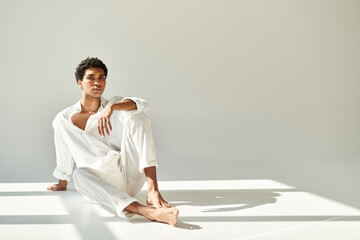 handsome sophisticated african american man in linen attire sitting on floor and looking at camera