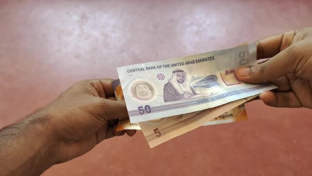 Two hands holding and exchanging united arab emirates dirham currency note with indian rupee notes. Closeup top view. International conversion, transaction, exchange, trade and commerce concept.