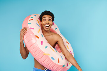 upbeat african american man posing with swimming ring on blue backdrop and looking at camera