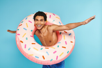 positive african american man posing with swimming ring on blue backdrop and looking at camera
