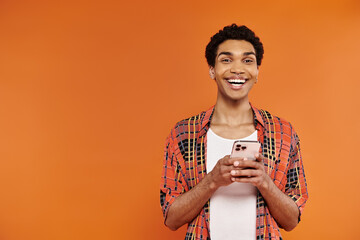 good looking joyous african american man in vibrant outfit holding smartphone and looking at camera