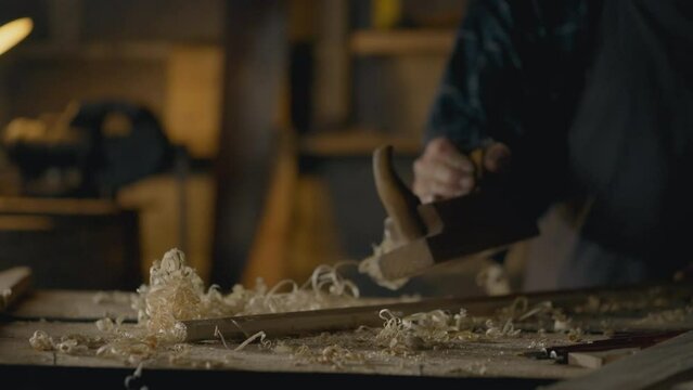 A woodworker works with a special woodworking tool using a planer, cutting dry wood into the desired shape. The process of processing wooden raw materials by the hands of a master