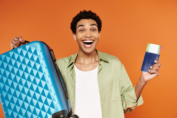 happy appealing african american man holding suitcase and passport with ticket and smiling at camera