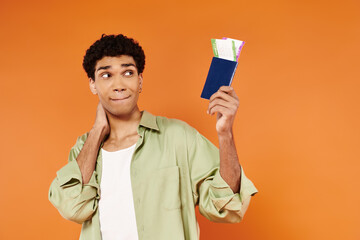 good looking jolly african american man looking at ticket and passport in hand on orange backdrop