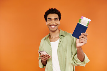 attractive merry african american man holding phone and passport with ticket and smiling at camera