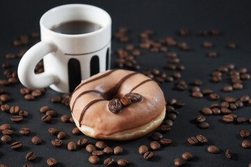 Caramel donut with coffee decoration next to a cup of black coffee on a dark background