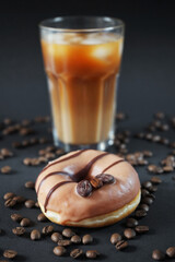 Caramel donut with coffee decor next to a glass of frappuccino with ice on a dark background