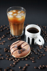 Caramel donut with coffee decoration next to a glass of iced frappuccino with a cup of black coffee on a dark background