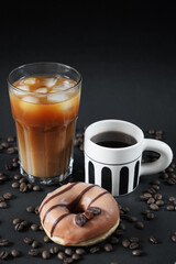 Caramel donut with coffee decoration next to a glass of iced frappuccino with a cup of black coffee on a dark background