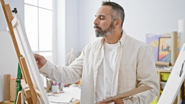 Focused mature man with grey beard painting in a bright art studio, portraying creativity and concentration.