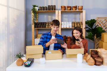 Couple of Caucasian male and Asian female sell vase products online live streaming at home. Packing vase parcels for send by order to customers. Remote purchase, Small business, Shopping online. - 783067703