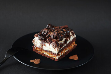 Chocolate cake with coffee flavor on a black plate next to a fork on a dark background