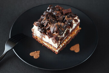Chocolate cake with coffee flavor on a black plate next to a fork on a dark background