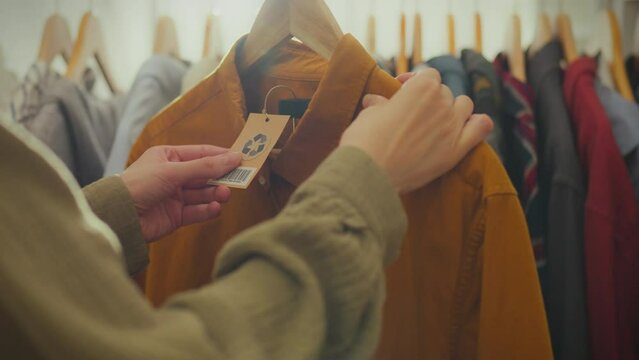 Cloth. Beautiful Asian girl holding a tag with a logo in a bright accessories store. Close-up of a fashionista girl looking at the recycling sign on the tag, following fashion trends and trends, store