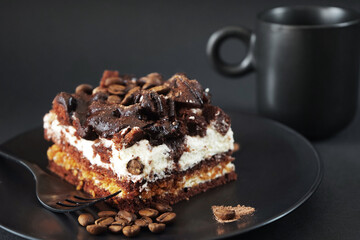 Chocolate cake with coffee flavor on a black plate next to a cup of coffee on a dark background