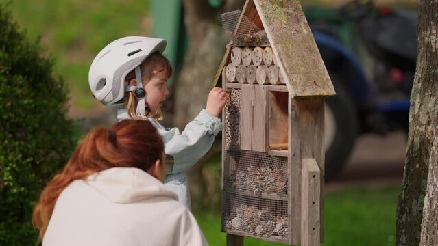 Mother and little daughter sitting beside insect hotel in kithcen garden and watch the insects
