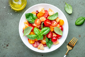 Simple italian salad with with stale bread, cherry tomatoes, olive oil, sea salt and green basil white plate, stone table background, top view - 783074531