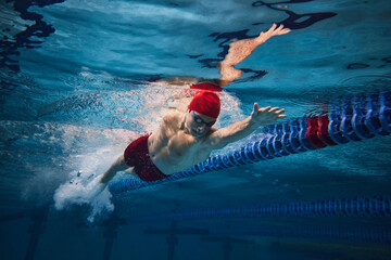 Powerful strokes. Freestyle swimming type. Young man, swimmer in motion training in swimming pool....