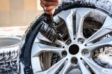 Man washing car's alloy wheels with brush.