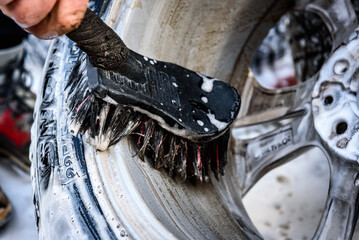 Man washing car's alloy wheels with brush.