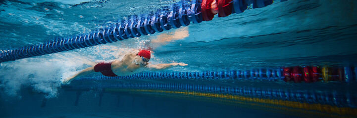 Young concentrated man, swimming athlete in motion in swimming pool training, preparing for...